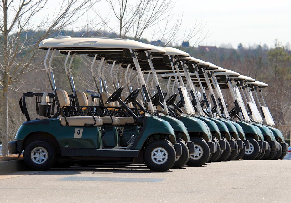 Multiple golf carts parked in a row on a golf course under a clear sky.